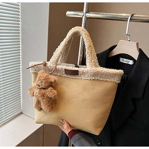Detail of yellow suede tote bag with faux fur trim and cute brown teddy bear keychain
