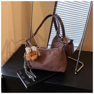 Détail d'un sac hobo en daim marron avec breloque nounours sur un bureau minimaliste