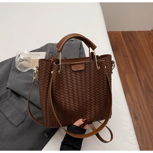 Close-up of brown woven bucket bag with metallic handle detail on a grey suit jacket