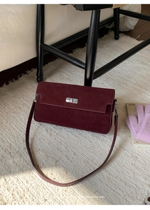 Close-up of burgundy suede envelope bag with a silver metal twist lock on a soft rug