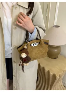 Detail of yellow suede bucket bag featuring leather handles and a knitted bear charm