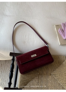 Detail of burgundy suede shoulder bag featuring a silver metal twist lock on the front flap