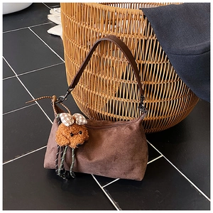 Détail d'un sac en daim marron avec un pendentif ours en peluche et bandoulière en cuir