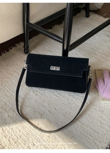 Detail of a black matte suede handbag with silver metal turn lock on a beige woven rug