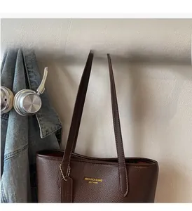 Deep brown pebble leather tote bag featuring gold logo and leather tag on wooden hook