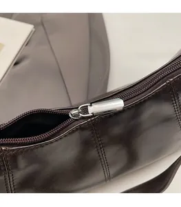 Close-up of smooth silver metal zipper pull and neat stitching on dark brown leather bag