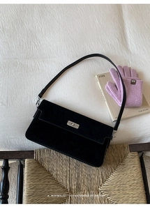 Close-up of black suede crossbody bag with silver metal twist lock on a white textured background