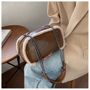 Detail of dark brown leather crossbody bag featuring ivory faux fur trim and gold chain strap