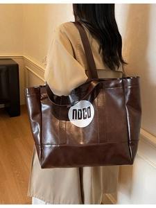 Brown faux leather tote bag with noco print worn over the shoulder with a beige coat