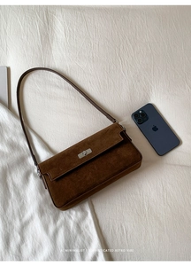 Detail of suede crossbody bag with vintage silver twist lock on soft white fabric