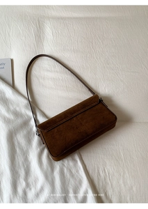 Close-up of retro brown suede shoulder bag with elegant silver hardware on white fabric