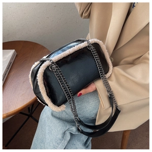 Detail of a black glossy shoulder bag with white faux shearling trim and metal chains