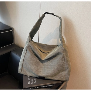 Minimalist grey canvas hobo bag with adjustable buckle strap on a black leather chair