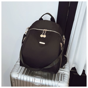 Close-up of black Oxford fabric backpack with gold metal logo on a silver suitcase