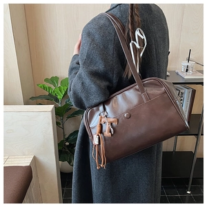 Detail of dark brown vintage faux leather shoulder bag with decorative tassel and T-pendant
