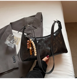 Detail of black faux leather hobo bag with vintage texture and wooden bead charm accessory