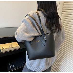 Détail d'un sac cabas en cuir noir grainé avec logo doré et double bandoulière