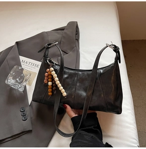 Detail of black faux leather dumpling bag with decorative wooden beads and stitching