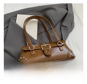 Gros plan d'un sac baguette rétro marron avec rivets métalliques sur une veste grise