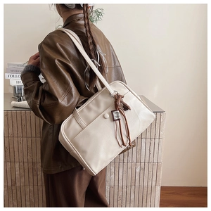 Detail of a beige leather shoulder bag with decorative brown cords and fashion tag