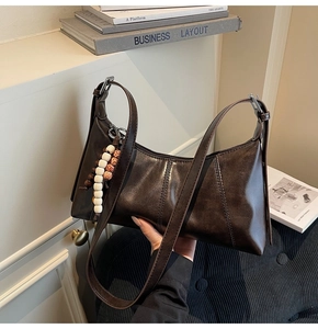 Detail of dark brown vintage faux leather shoulder bag with a beaded wooden charm