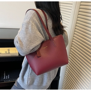 Detail of dark red lychee grain leather tote bag with gold logo on model's shoulder