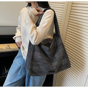 Close-up of a large textured dark grey tote bag worn by a model in a casual setting