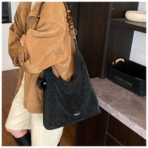 Détail du sac hobo noir avec bandoulière unique en perles de bois marron et pompon