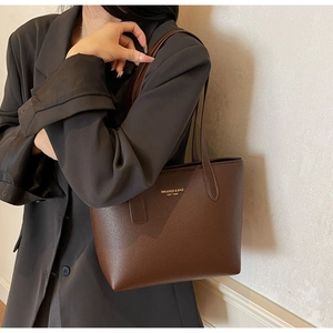 Détail de la texture cuir litchi marron foncé et logo doré sur un sac cabas chic