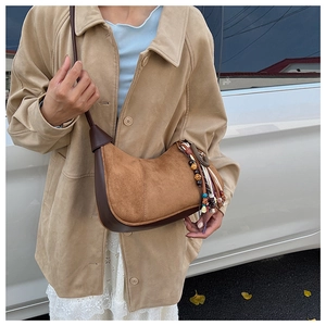 Détail du sac bandoulière en daim avec pompon vintage porté sur une veste décontractée
