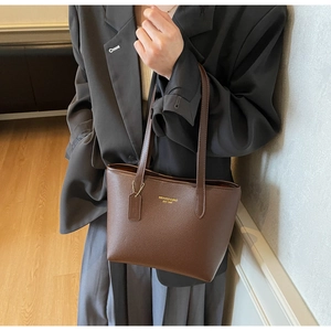 Détail du sac cabas en cuir marron foncé avec lettrage doré porté par le mannequin