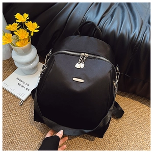 Detail of black oxford backpack showing metal zippers, logo plaque and chain straps