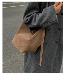 Brown suede shoulder bag with metal eyelet strap detail worn over a grey coat
