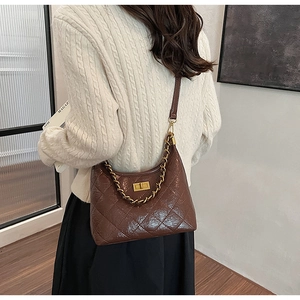 Détail du sac matelassé marron foncé avec chaîne dorée et fermoir pivotant sur l'épaule