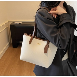 Gros plan sur le sac cabas crème avec poignées brunes et logo porté par un mannequin