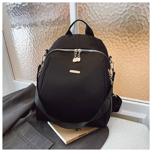 Detail of black nylon backpack with gold hardware and logo on a gray suit background