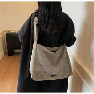 Lifestyle view of a large grey-brown textured tote bag with a wide crossbody strap