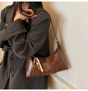 Detail of vintage brown leather dumpling bag with artistic beaded pendant on side