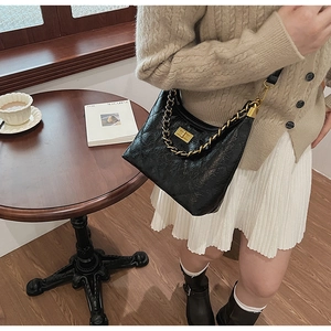 Sac en cuir noir matelassé avec chaîne dorée présenté dans un décor de café chaleureux