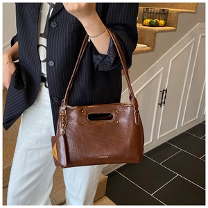 Detail of dark brown wax leather tote with gold rivets and mini charm on a model