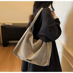 Close-up of a large taupe canvas tote bag with wide strap on a model's shoulder