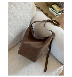 Detail view of brown suede shoulder bag with silver metal ring and wide strap on white sofa
