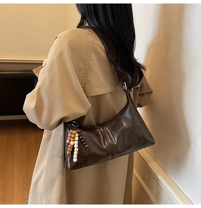 Detail of dark brown leather crescent bag with colorful wooden beaded charm on a model