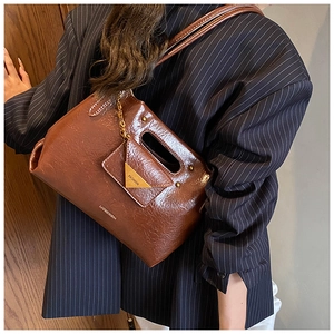 Detail of retro oil-waxed brown leather handbag with gold metal logo and chain strap