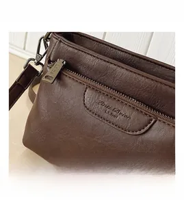 Detail shot of a dark brown leather crossbody bag with double zippers and fine stitching