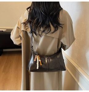 Detail of dark brown vintage crossbody bag with colorful wooden bead charm and stitching