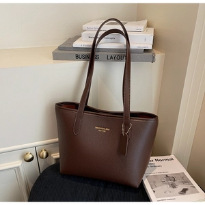 Close-up of deep brown lychee texture leather tote with gold logo and shoulder strap