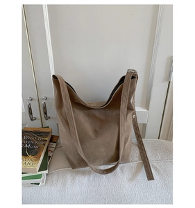 Detail of a dark brown suede tote bag featuring a wide shoulder strap and metal ring buckle