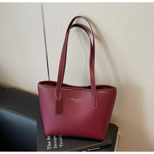 Close-up of burgundy lychee grain leather tote bag with gold logo and matching hangtag