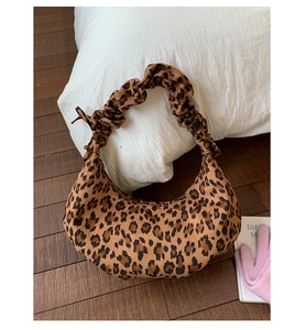 Detail of leopard print suede hobo bag with ruched handle on warm wooden floor